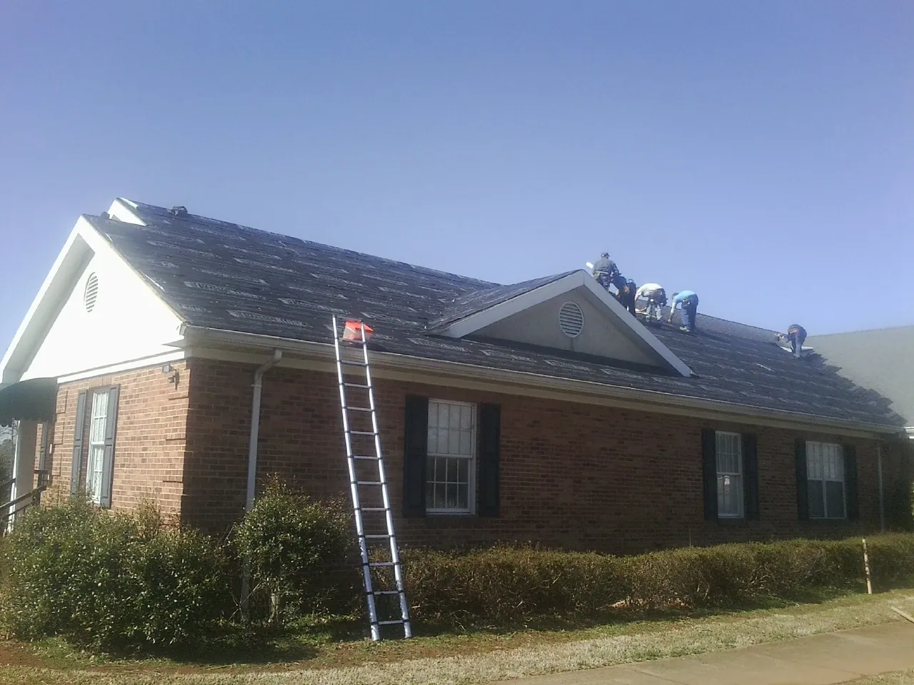 Crew tearing shingles off a brick ranch roof with a ladder set — Emergency Roof Repair work by our crew in Smithmill