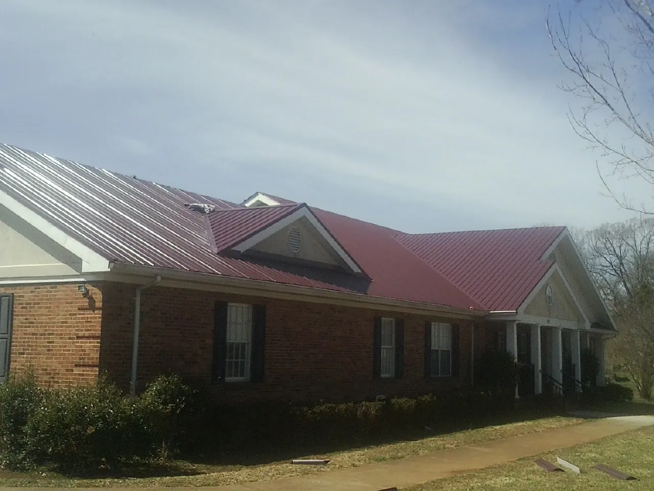 Red metal roof with gabled entries on a long brick building, from a Hail Damage Roof Repair job in Smithmill