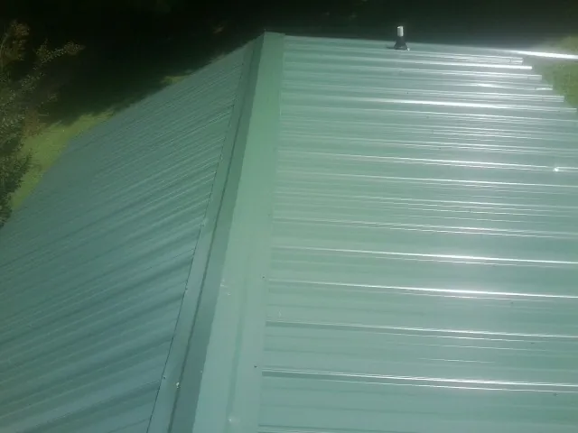 New green metal panels meeting at the ridge of a roof — Flat Roof Repair work by our crew in Smithmill