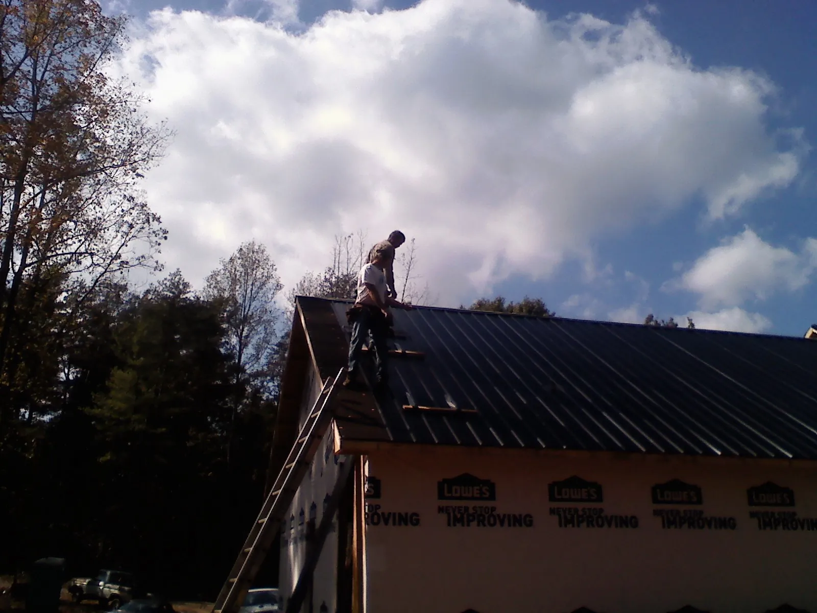 Roofer fastening dark metal panels high against a cloudy sky, from a Roof Inspection job in Smithmill